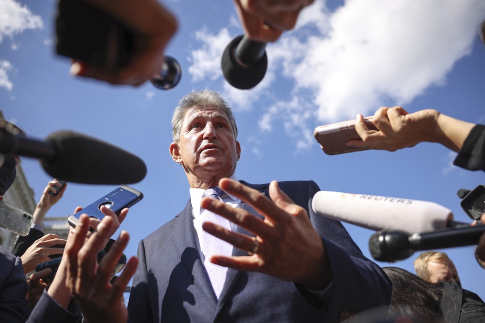 Senator Joe Manchin walks outside surrounded by reporters and recording devices.