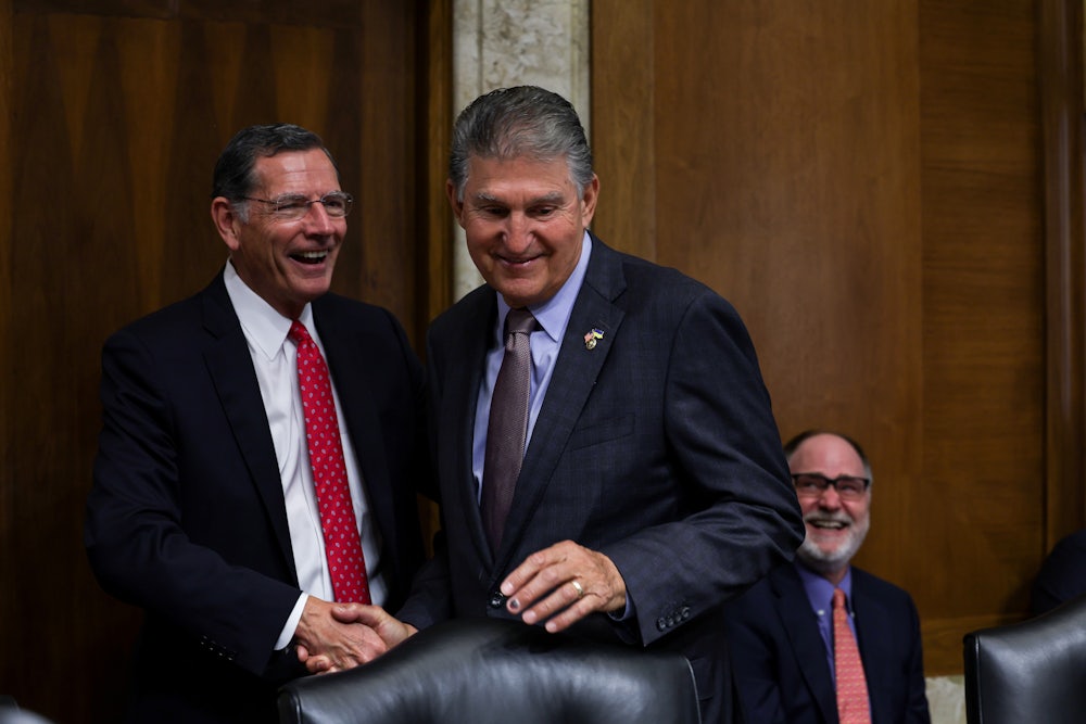 Joe Manchin smiles while shaking hands with Senator John Barrasso.