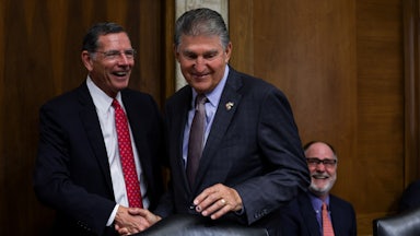 Joe Manchin smiles while shaking hands with Senator John Barrasso.