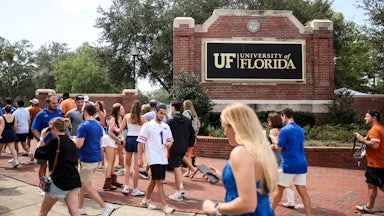 Fans in blue walk in front of a large "University of Florida" sign.