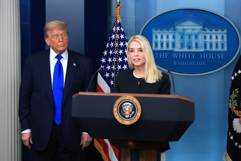 Donald Trump listens as Attorney General Pam Bondi speaks behind the lectern in the White House's press briefing room.