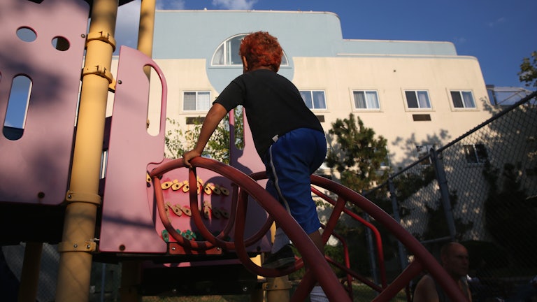 A child with bright red hair and blue pants climbs a ladder at a playground.