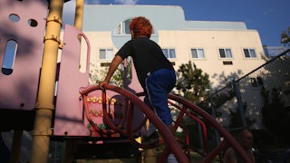 A child with bright red hair and blue pants climbs a ladder at a playground.