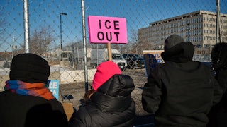 A protester holds an "ICE OUT" sign outside a detention center.
