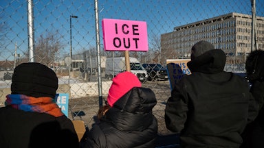 A protester holds an "ICE OUT" sign outside a detention center.