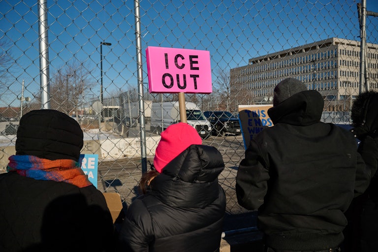 A protester holds an "ICE OUT" sign outside a detention center.