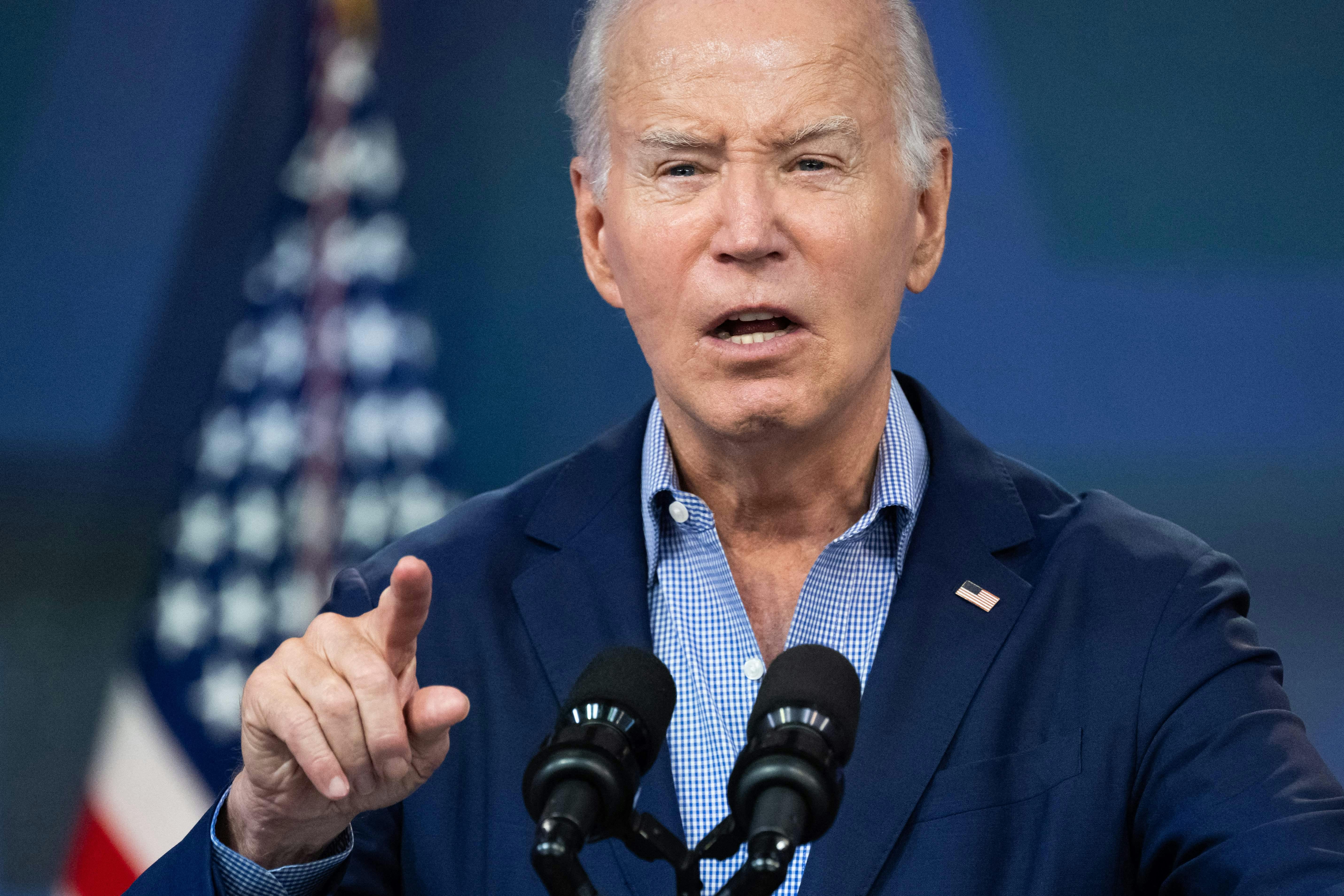 Joe Biden lifts his finger while speaking into microphones.