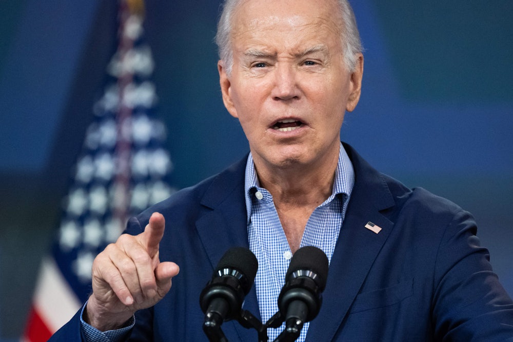 Joe Biden lifts his finger while speaking into microphones.
