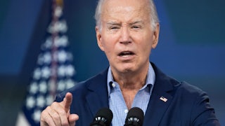 Joe Biden lifts his finger while speaking into microphones.
