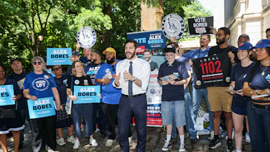 Alex Bores stands in front of a crowd of supporters holding signs.