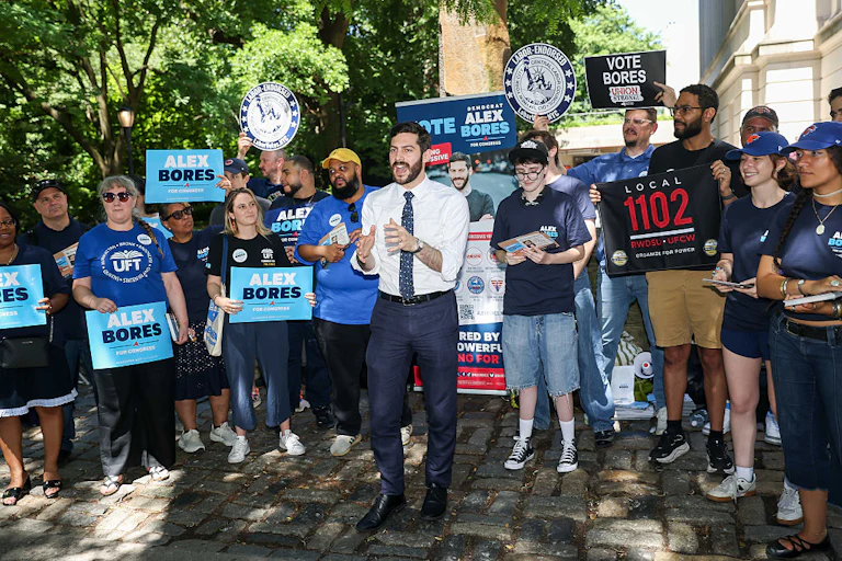 Alex Bores stands in front of a crowd of supporters holding signs.