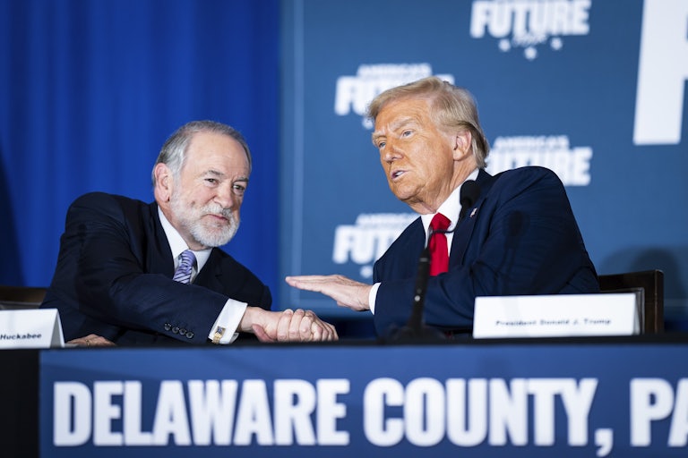 Mike Huckabee and Donald Trump shake hands while sitting at a table