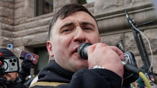 Jake Lang speaks into a microphone while outdoors.