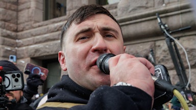 Jake Lang speaks into a microphone while outdoors.
