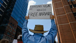 A protester holds a sign that reads "Strong USA Needs Free Harvard."