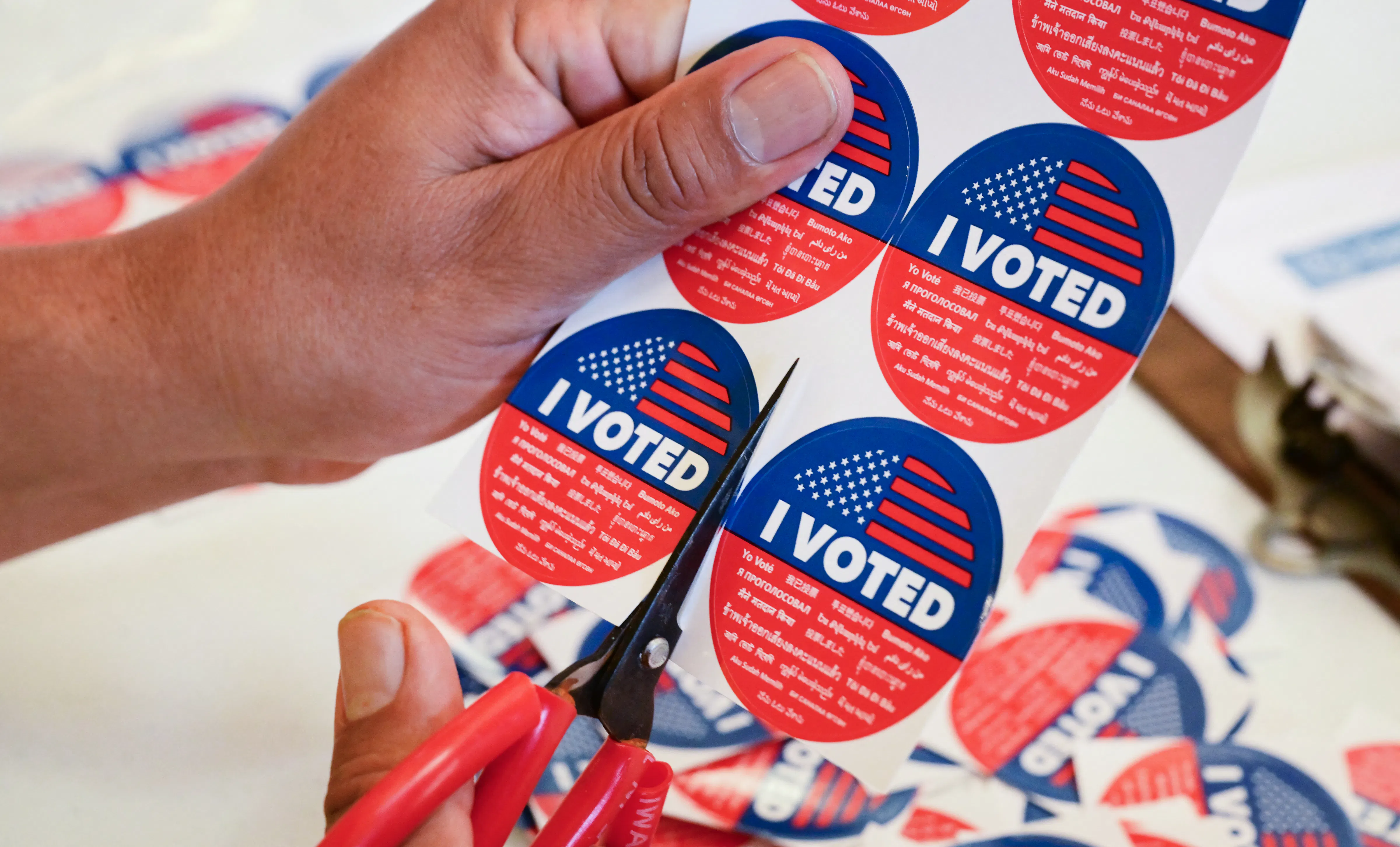 A person cuts up a sheet of "I voted" stickers with a pair of scissors