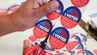 A person cuts up a sheet of "I voted" stickers with a pair of scissors