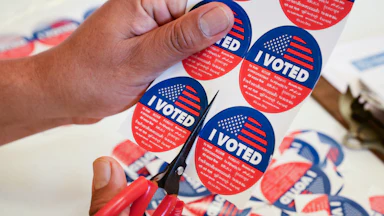 A person cuts up a sheet of "I voted" stickers with a pair of scissors
