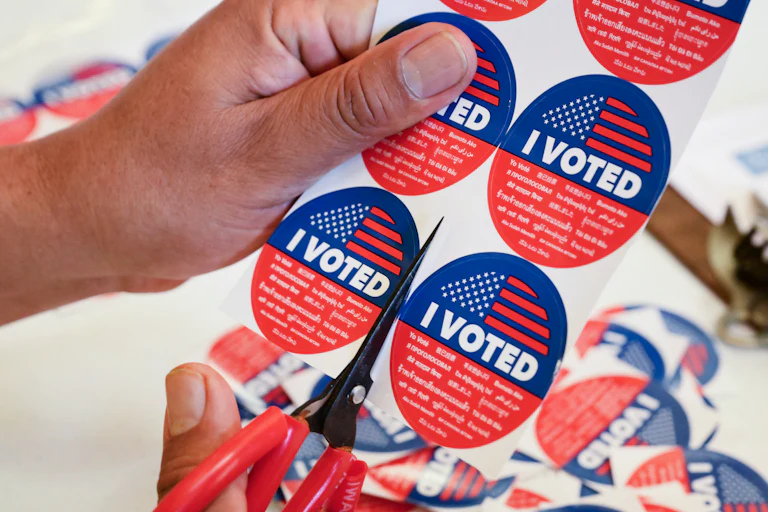 A person cuts up a sheet of "I voted" stickers with a pair of scissors