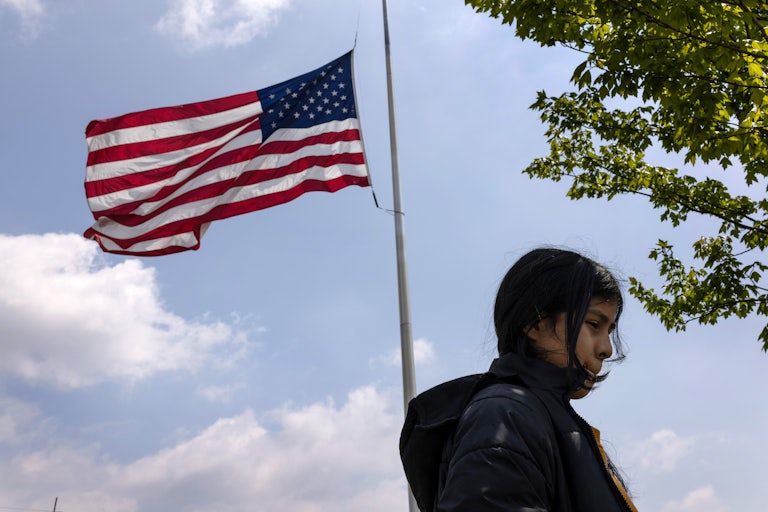 A ten-year old immigrant from Honduras stands underneath the American flag in a public park.