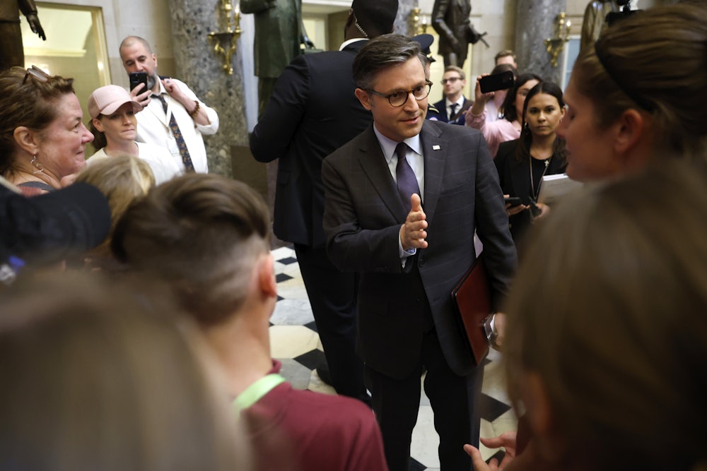 Mike Johnson stands in a group of people and gestures while talking.