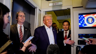 Donald Trump shrugs aboard Air Force One, as Scott Bessent and Marco Rubio stand on either side of him. Reporters surround them, holding their phones out to record.