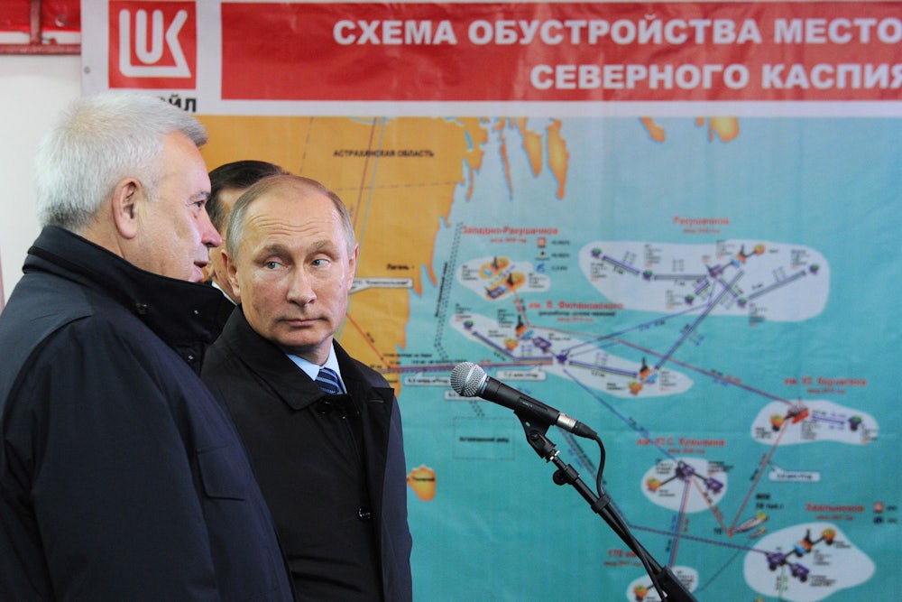 Vladimir Putin stands in front of an oil schematic while listening to another man talk.
