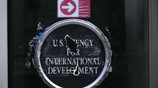 U.S. Agency for International Develoment logo on a glass door. Holes blocks out parts of the words "Agency" and "Development."