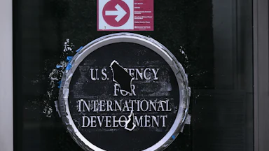 U.S. Agency for International Develoment logo on a glass door. Holes blocks out parts of the words "Agency" and "Development."
