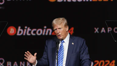 Donald Trump speaks in front of a bitcoin2024 backdrop.