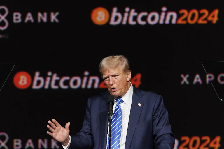 Donald Trump speaks in front of a bitcoin2024 backdrop.