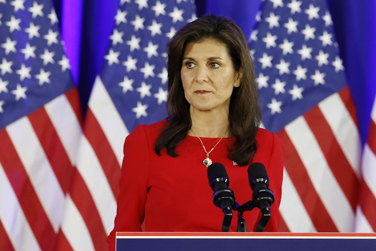 Nikki Haley looks nervously off camera. U.S. flags are behind her and mics on a lectern are before her.