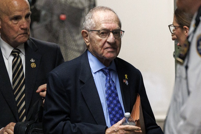 Alan Dershowitz holds a file folder and walks outside a Manhattan courthouse