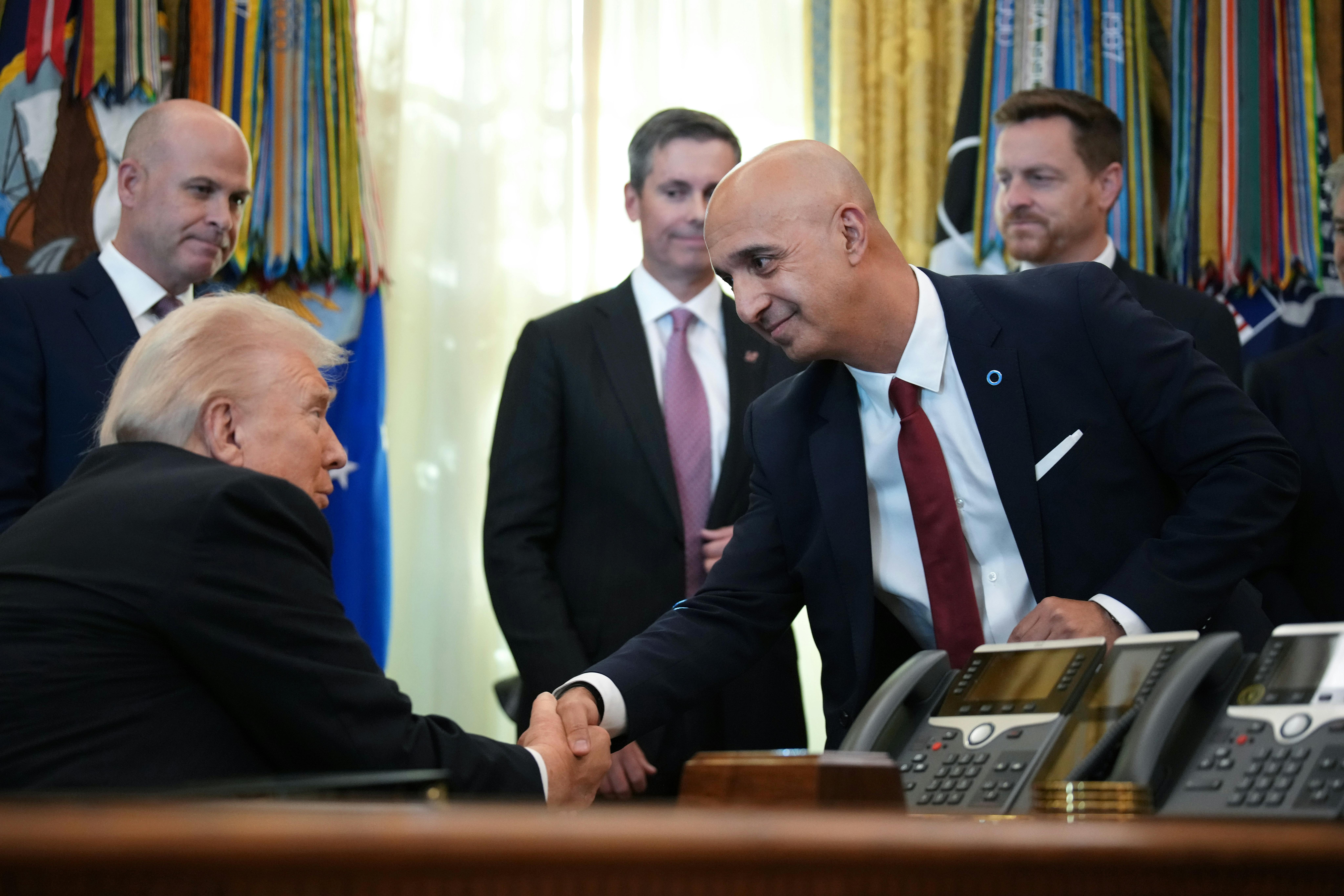 Novo Nordisk CEO Mike Doustdar bends down to shake hands with Donald Trump, who is seated behind his desk in the White House Oval Office.