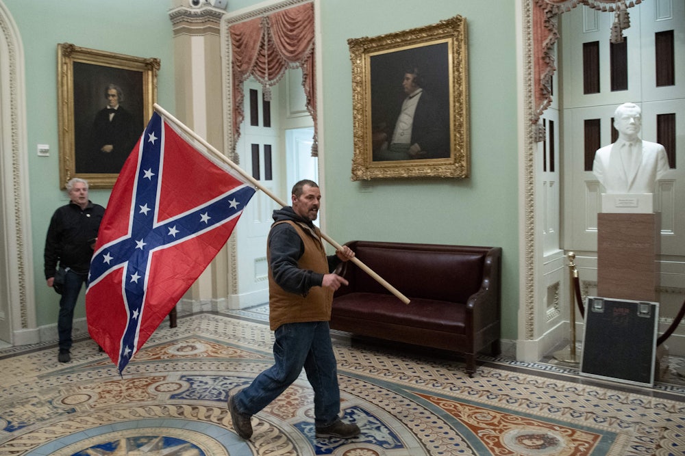 A man in a vest carries a Confederate flag over his shoulder in a room hung with historical portraits.