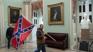 A man in a vest carries a Confederate flag over his shoulder in a room hung with historical portraits.