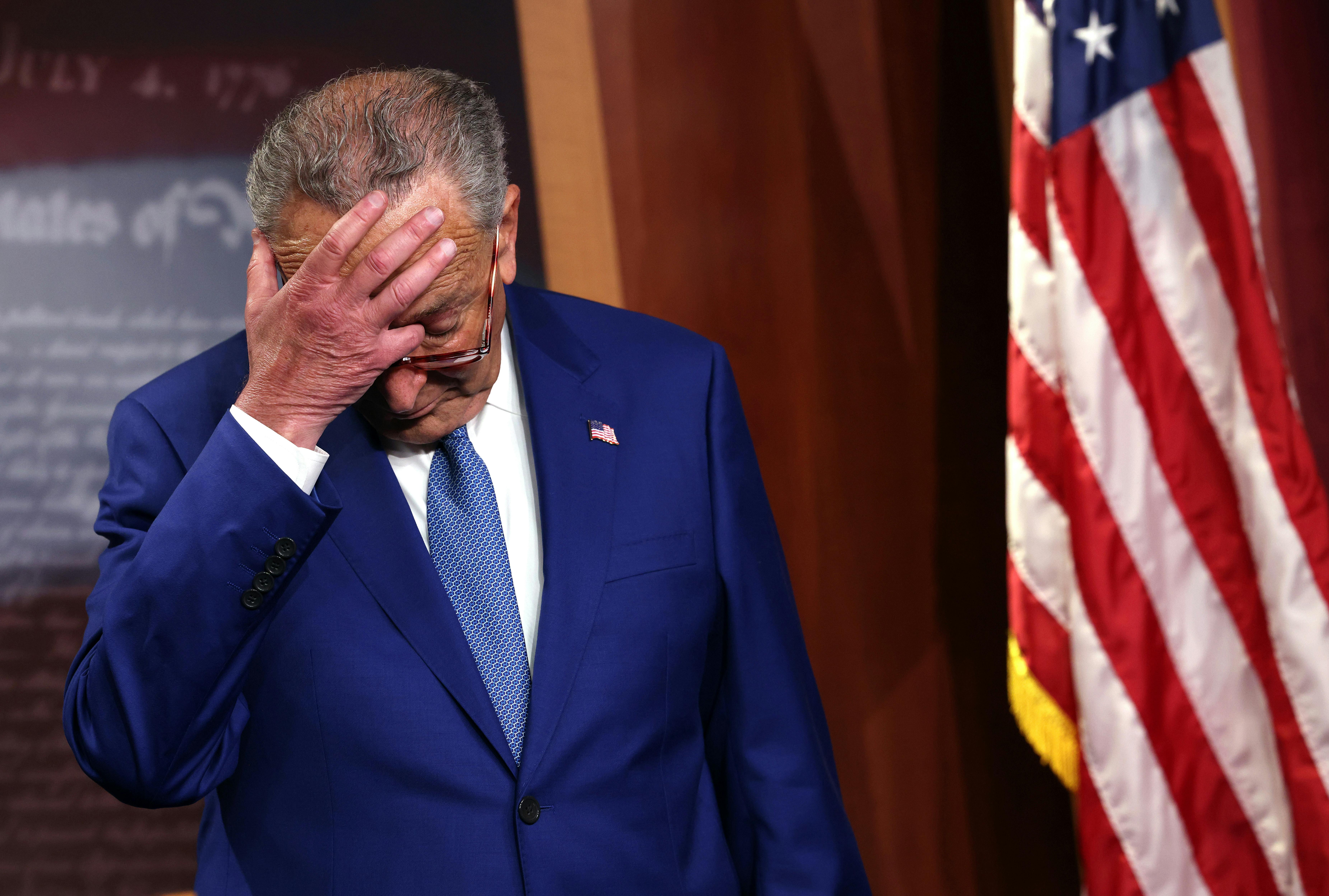 Senate Majority Leader Charles Schumer scratches his head as he attends a press conference.