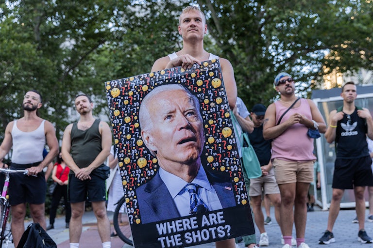 A demonstrator holds a picture of President Biden with text beneath reading "Where are the shots?"