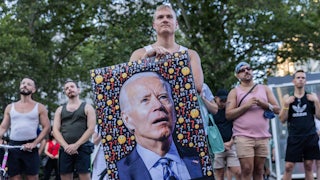 A demonstrator holds a picture of President Biden with text beneath reading "Where are the shots?"