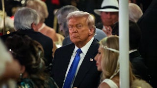 Donald Trump sits in a crowd looking grumpy.