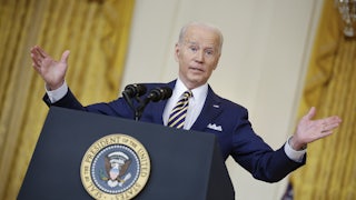 President Joe Biden stands behind a lectern, shrugging.