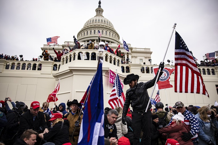 Pro-Trump rioters climb on the Capitol on January 6, 2021. Many wave Trump and U.S. flags.