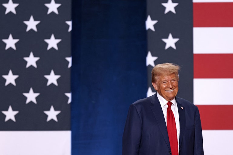 Donald Trump smiles in front of U.S. flags