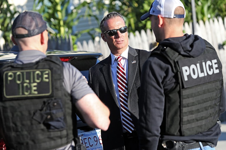 Todd Lyons stands with two police officers, one of whom wears a vest that reads "POLICE ICE."