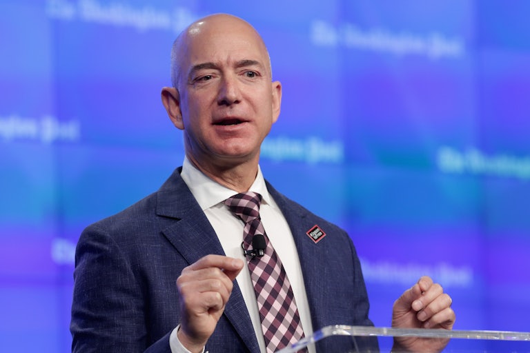 Jeff Bezos speaks at a lectern while behind him is a banner that reads The Washington Post.