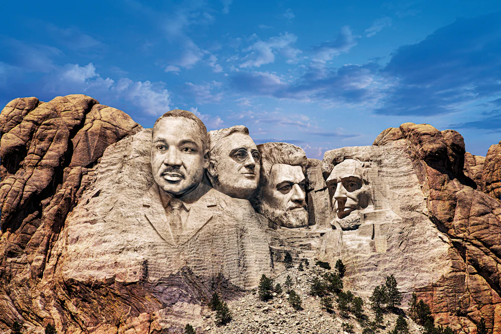 A digitally altered photograph of Mount Rushmore depicting four faces carved into the mountain in place of the original presidents. From left to right: a figure resembling Martin Luther King, FDR, Frederick Douglass, and Lincoln.