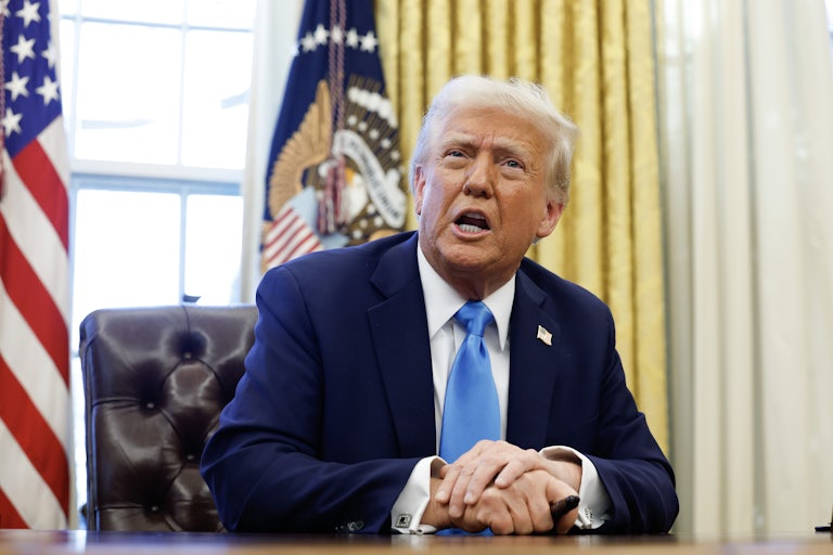 Donald Trump speaks to reporters while sitting at his desk in the Oval Office