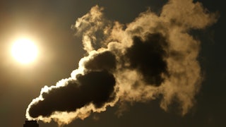 Smoke billows across the sky with the sun in the background.