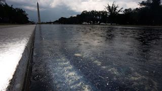 A low view of the Lincoln Memorial Reflecting Pool in the rain, with chipped paint and algae visible. In the background, the Washington Monument can be seen.