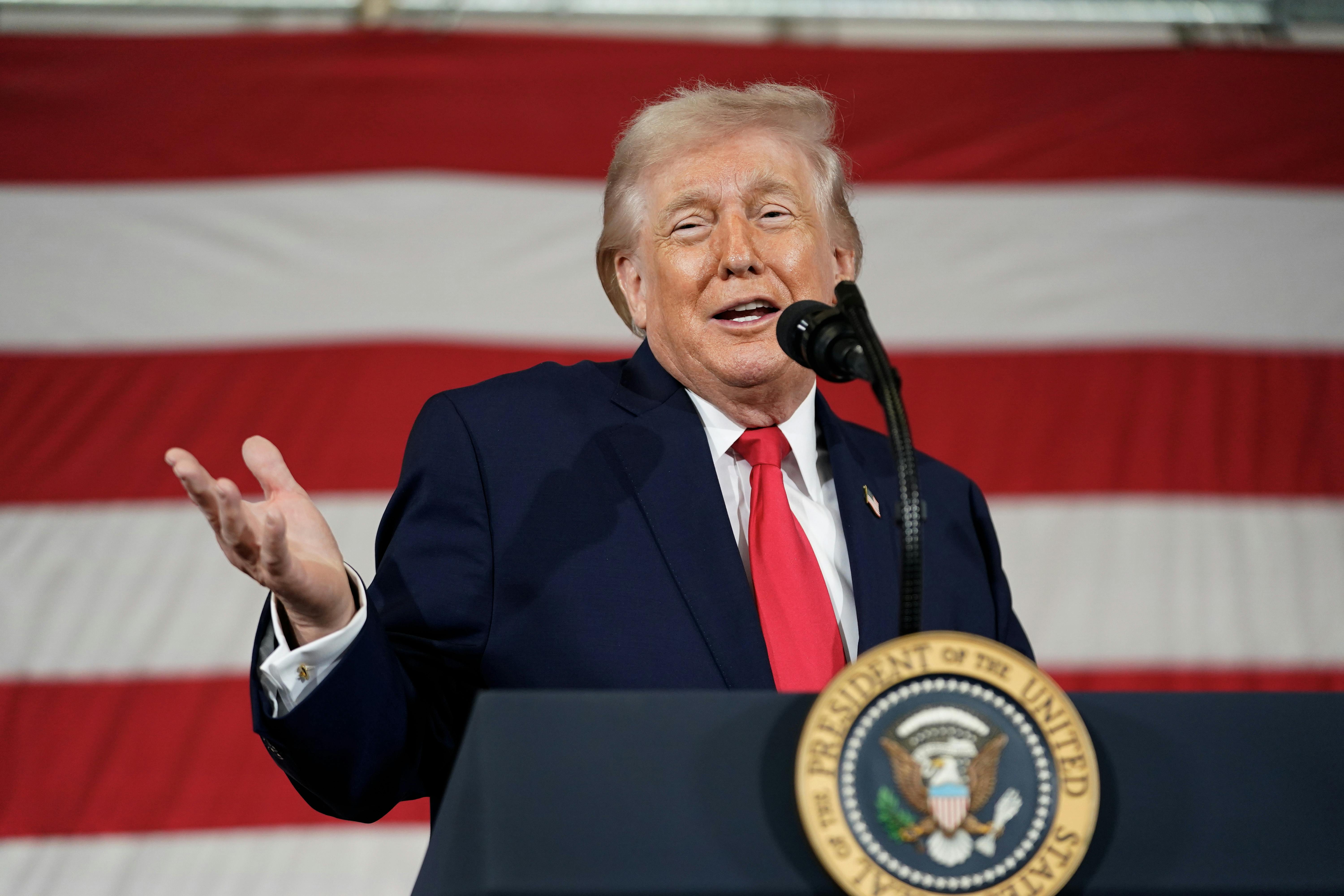 Donald Trump holds his hand out and smiles while speaking behind a lectern 